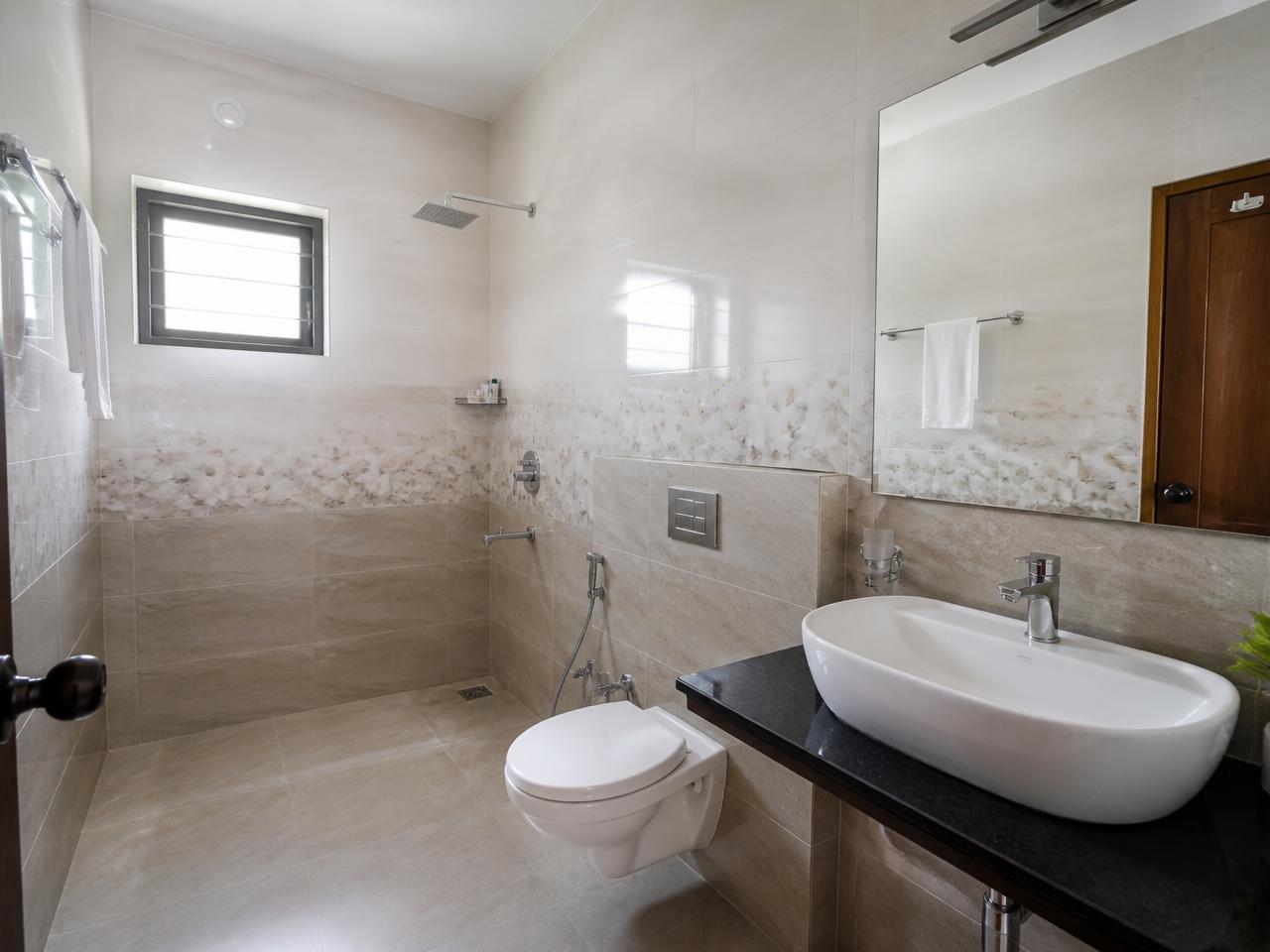 Tiled attached bathroom with shower area, mirror and wash basin